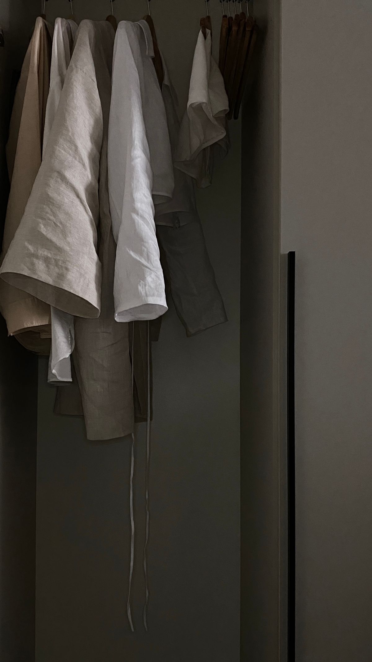 Linen clothes hanging on wooden hangers in a softly lit wardrobe.