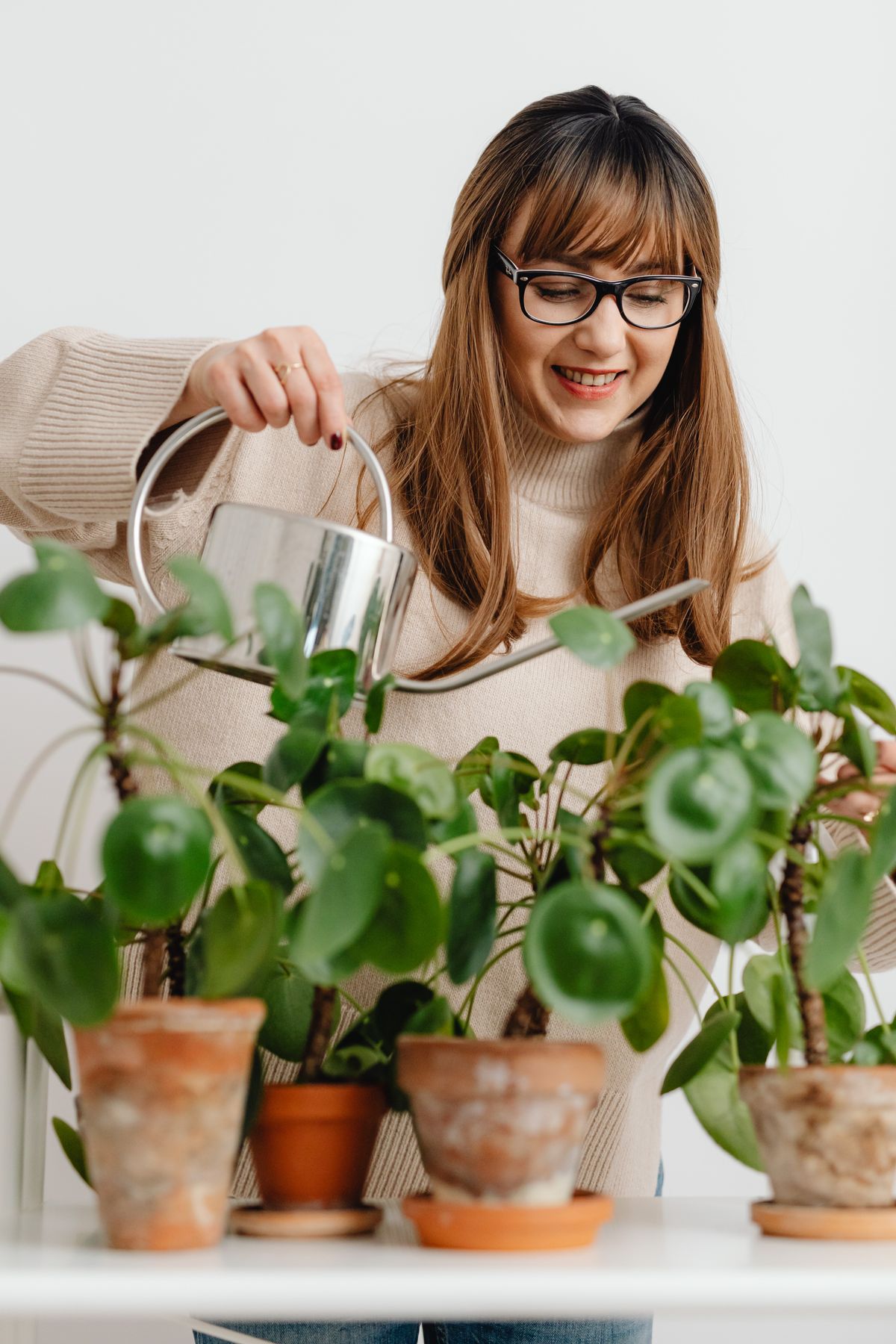 A smiling woman watering leafy houseplants at home.